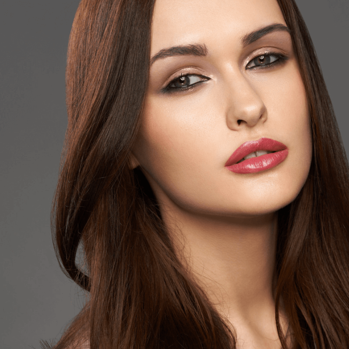 Bilde av en kvinne med lang, brun hår og naturlig make-up, som viser et friskt og elegant utseende.