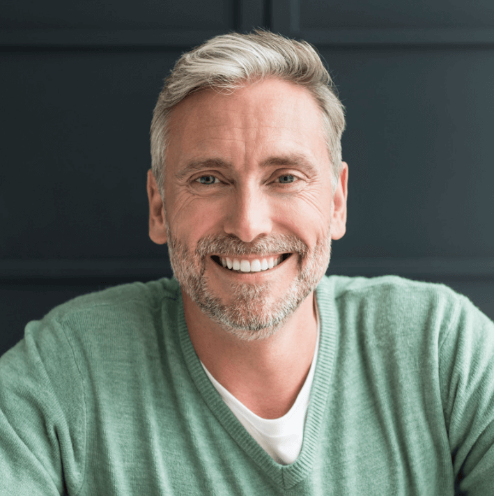 Smiling middle-aged man wearing a green sweater, with a friendly expression and healthy skin.